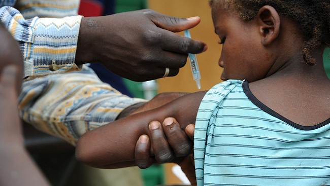 Child getting a vaccine. Photograph shows adult and holding the arm of a girl while she is getting vaccinated with a needle.
