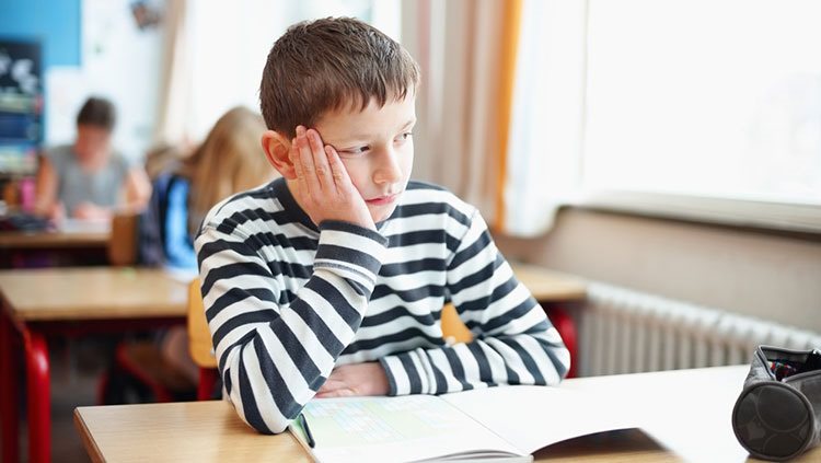 Boy sitting at desk with hand on face