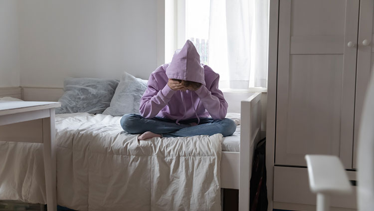 Teenage sitting on bed with legs crossed and hands in head