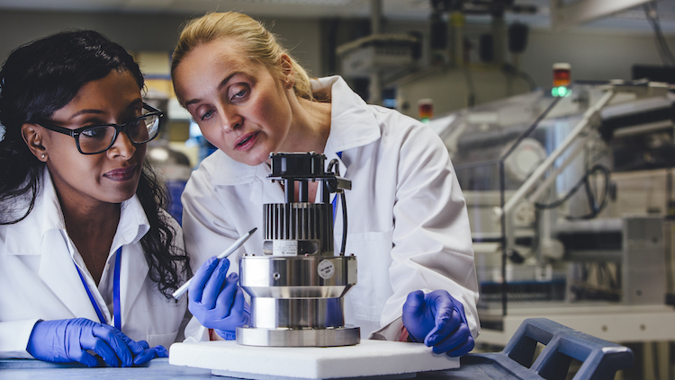 Photograph of two female scientists in lab coats looking at an experiment