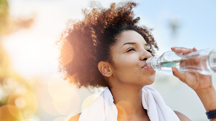 Woman drinking from water bottle with towel around her neck