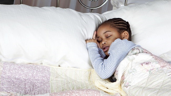 Photo of a girl sleeping in a bed, heading resting on a pillow.