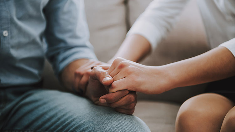 Closeup of two people sitting on a couch and holding hands